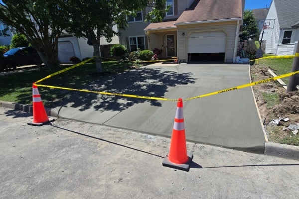 Freshly poured concrete driveway marked with traffic cones and caution tape, situated in front of a house.