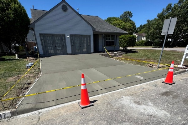 Freshly poured concrete driveway in front of a house, marked off with caution tape and traffic cones.