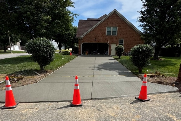 Freshly poured concrete driveway with traffic cones marking the edges, and a brick house in the background.