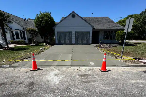 Newly poured concrete driveway in front of a house, marked with caution tape and orange traffic cones.