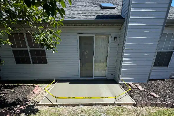 Newly poured concrete patio with caution tape around it, adjacent to a house with sliding glass doors.