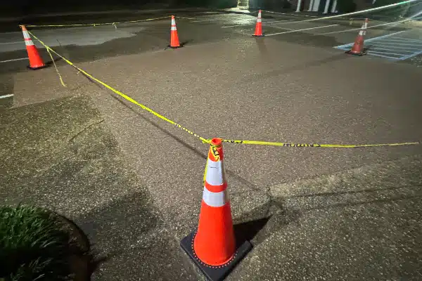 Five orange traffic cones are set up around a section of pavement, cordoned off with yellow caution tape at night.