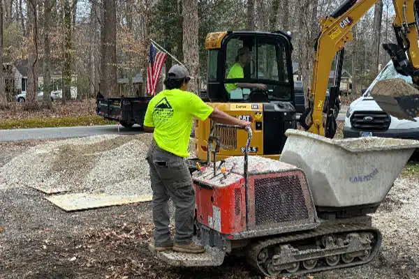 Construction workers operate machinery and prepare gravel in a wooded area, with an American flag visible.