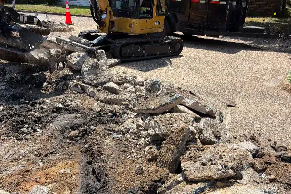 Heavy machinery on a construction site with broken concrete and gravel piles, surrounded by a dirt area.