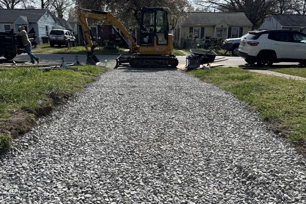 Gravel pathway leading toward a construction vehicle, with tools and equipment nearby in a residential area.
